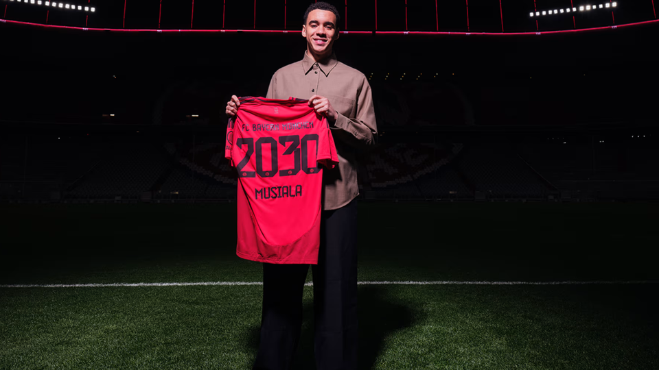 Foto do anúncio de renovação de Musiala com o Bayern, segurando a camisola com o número 2030, validade do contrato