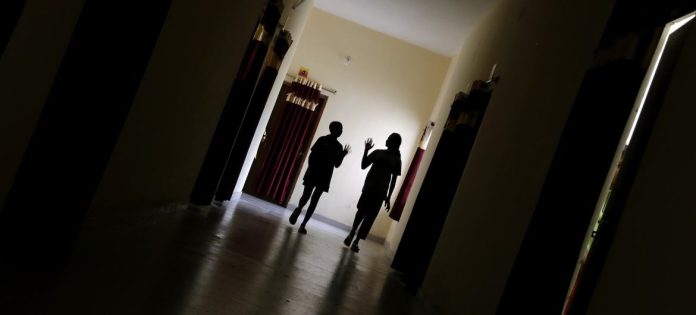 Duas meninas, de 13 e 15 anos, caminham pelo corredor para participar de uma sessão de grupo psicossocial em Dantewada, Chhattisgarh, Índia