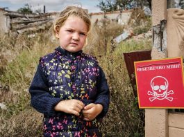 Veronika, de 4 anos, está perto de uma placa que diz "Perigo de Minas"