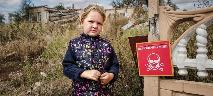 Veronika, de 4 anos, está perto de uma placa que diz "Perigo de Minas"