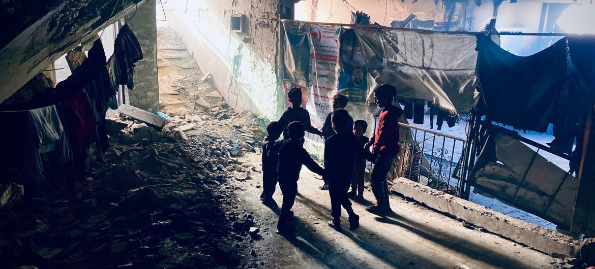 Uma família caminha por uma área onde as pessoas estão abrigadas nos restos de um edifício bombardeado em Gaza Uma família caminha por uma área onde as pessoas estão abrigadas nos restos de um edifício bombardeado em Gaza